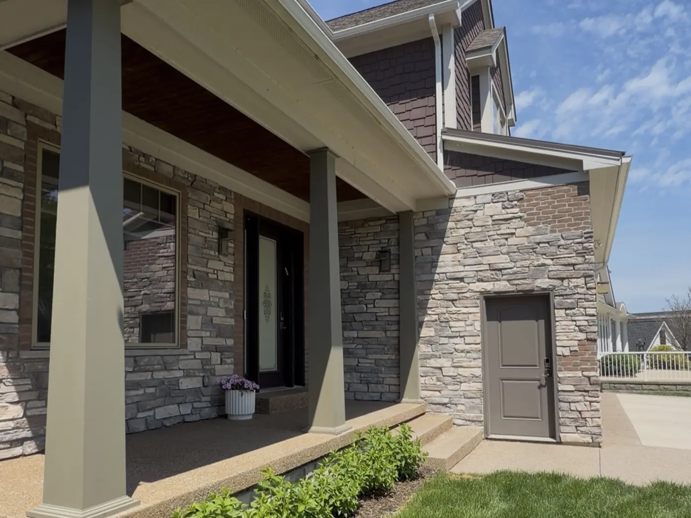 Covered porch before painting: taupe columns, a dark stained ceiling, and brown trim around the side door.