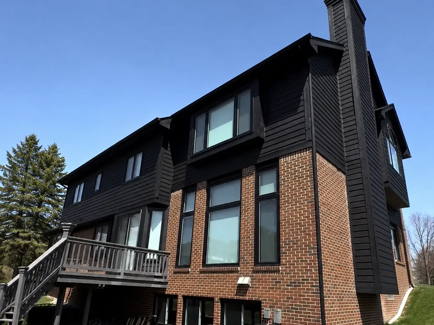 The same rear elevation after painting: siding, window surrounds, chimney, and deck in matte black against the brick and the lawn.