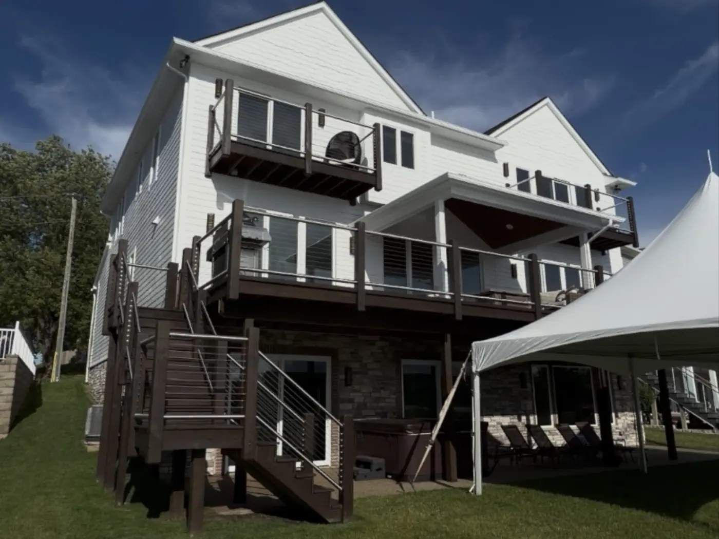 The same rear elevation after painting: siding and gables in a uniform white that lifts the stone base and the dark deck rails.