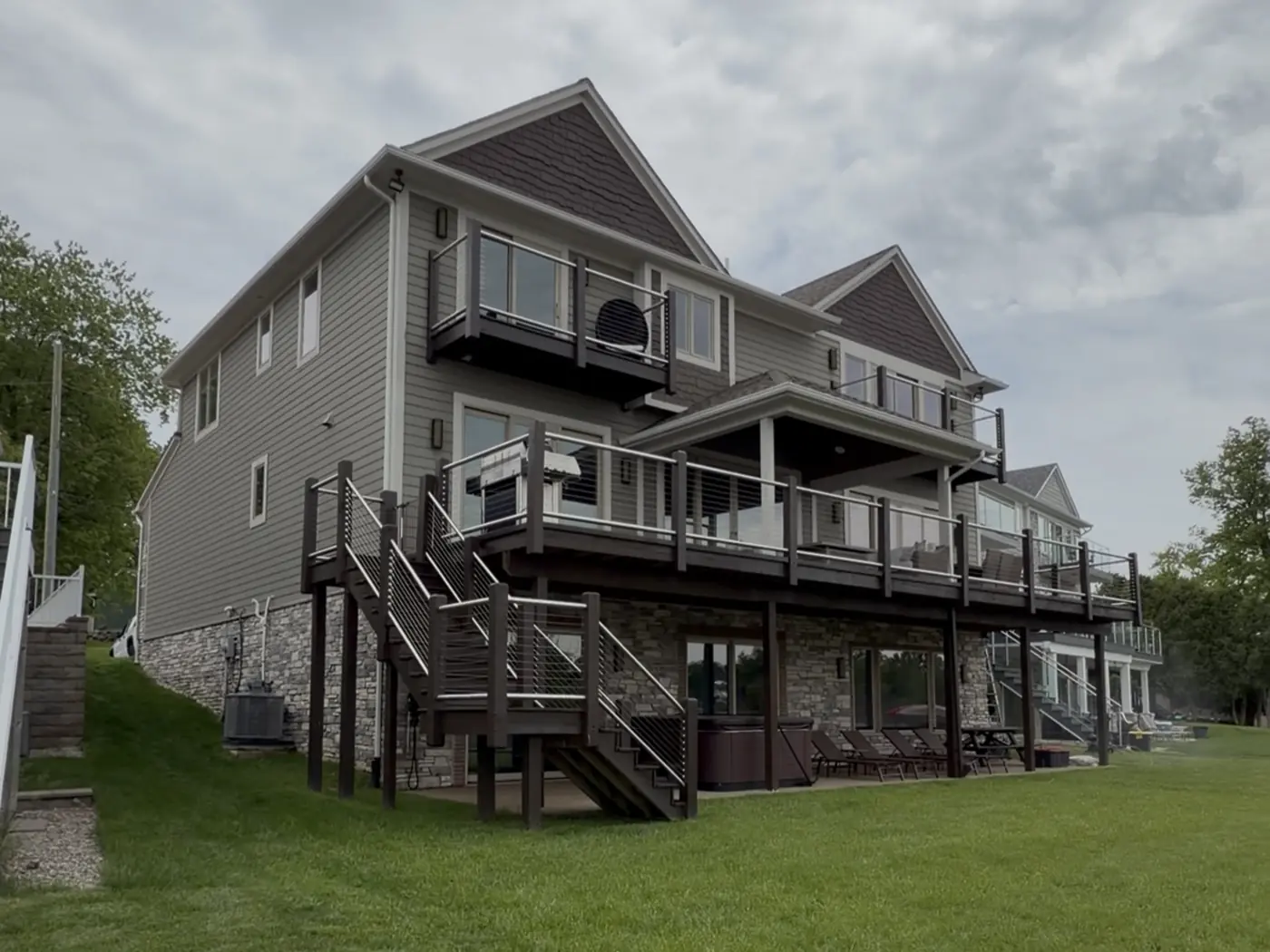 Rear of a lakeside house before painting: tan siding and brown gable shingles across three storeys of stacked decks.